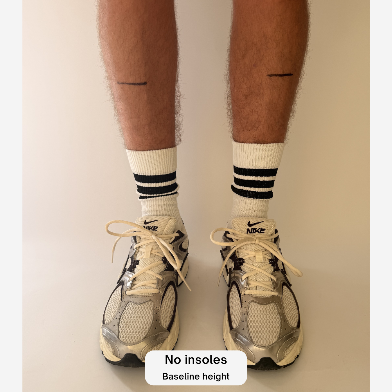 A person's legs and feet wearing white Nike socks with black stripes and white and gray Nike running shoes, standing against a plain beige background. A text overlay at the bottom reads 'No insoles in'.
