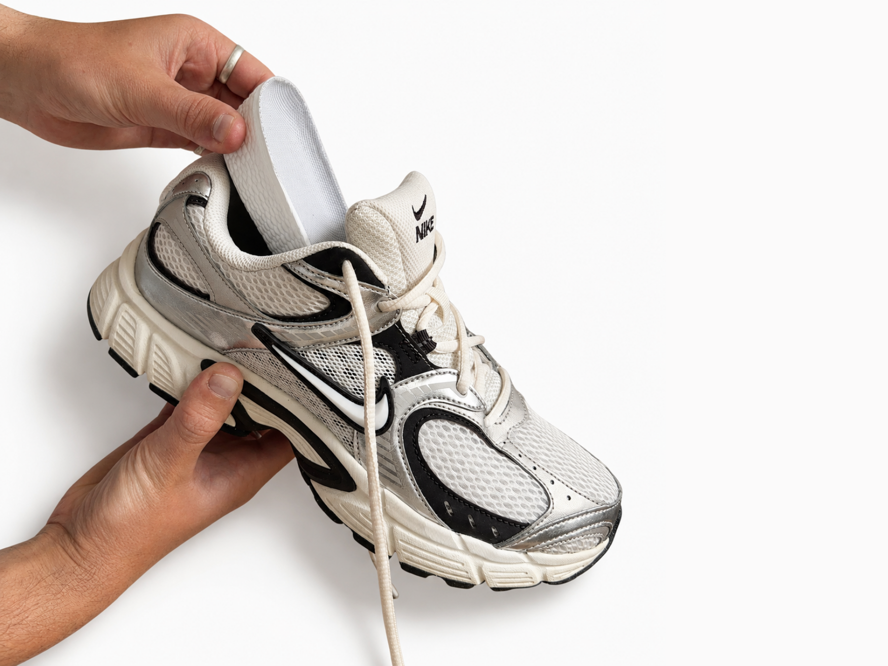 Person holding up a white and black nike sneaker whilst inserting an White Ondorq Elevate height increasing insole on a white background