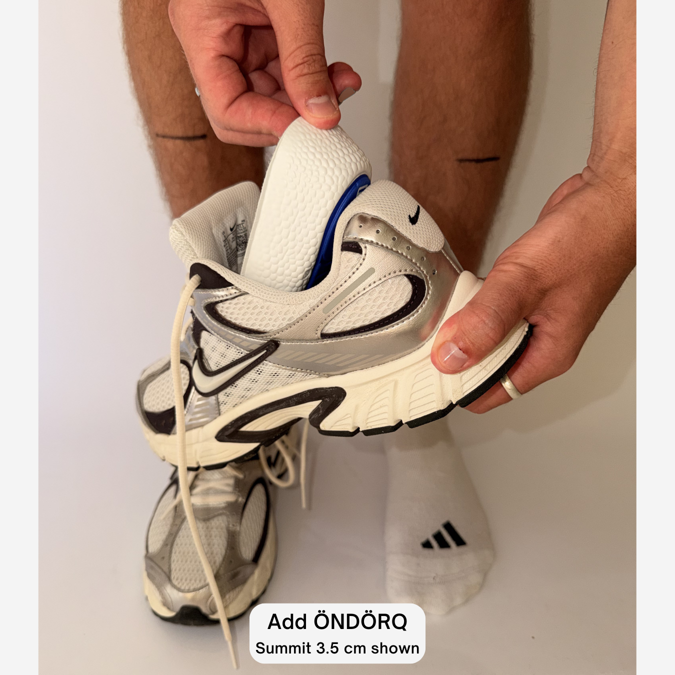 A person holding a white and black running shoe and adding an Öndörq Elevate invisible height insoles for men.
